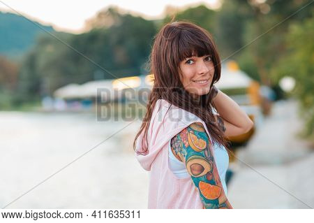 Summertime. Portrait Of A Pretty Happy Woman With A Tattoo On Her Arm, Posing In A Half-turn. Embank