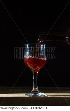 Homemade Red Wine Is Poured Into A Glass On A Dark Background. Glass Of Red Wine On A Black Backgrou