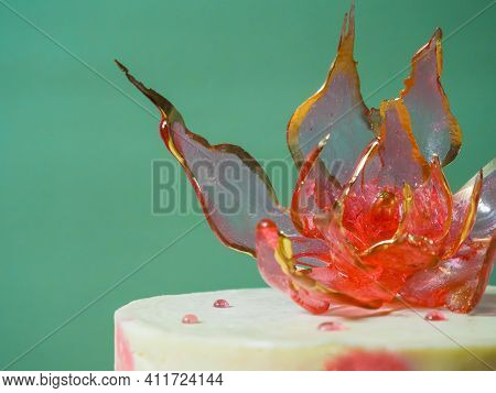An Edible Red Isomalt Flower On Top Of A Cake On A Pale Green Background