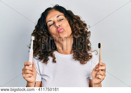 Middle age hispanic woman holding electric toothbrush and teethbrush looking at the camera blowing a kiss being lovely and sexy. love expression. 