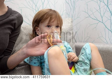 Kid Girl Makes Inhalation With A Nebulizer. Sick Child Holding Inhalator In Hand And Breathes Throug