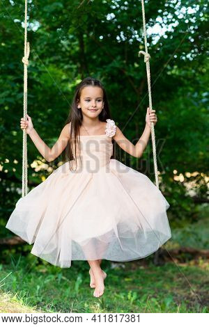 Happy girl rides on a swing in park. Little Princess has fun outdoor, summer nature outdoor. Childhood, child lifestyle, enjoyment, happiness.