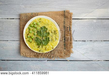 Cracked Wheat Khichdi Or Khichuri In A Plate With Coriander Leaves And Green Pea On Burlap Fabric Is
