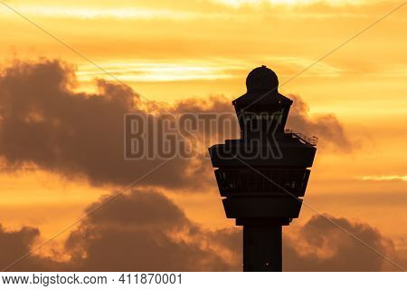 International Airport Control Tower With A Plane Landing In The Background During Sunset.