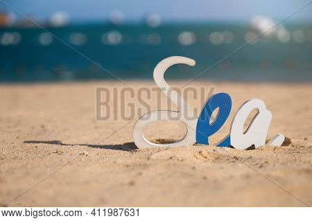 Decorative Sea Inscription, Woodenl Letters On The Beach In The Sand Against The Background Of The S