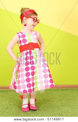 Mod little girl in a bright dress and large red glasses, hands on belt