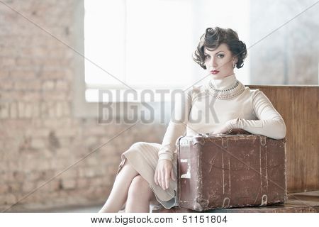 Beautiful vintage style young woman with suitcase on a train station