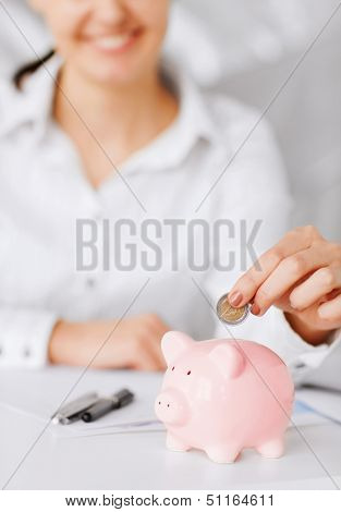 business, office, household, school, tax and education concept - woman hand putting coin into small piggy bank