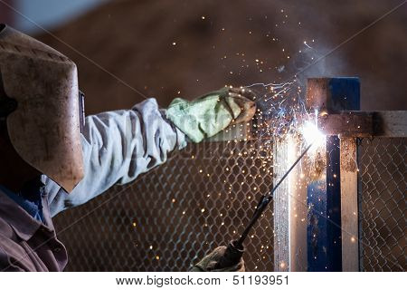 Heavy industry welder worker in protective mask hand holding arc welding torch working on metal construction