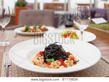 Black squid ink pasta with seafood and other dishes on restaurant table