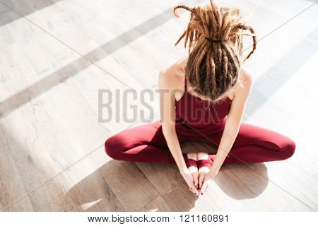 Top view of modern young woman with dreadlocks sitting and doing yoga on wooden floor