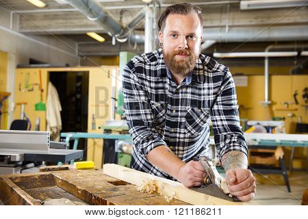 Smiling carpenter work with plane on wood plank in workshop