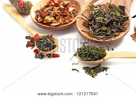 Different sorts of dry tea in wooden spoons, isolated on white