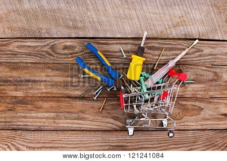 Shopping cart with construction tools on the old wood background. Toned image.