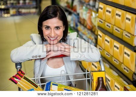 Smiling woman leaning on troller in supermarket