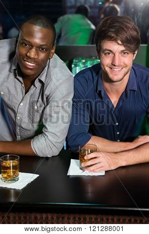Portrait of two men smiling while having whiskey at bar counter in bar