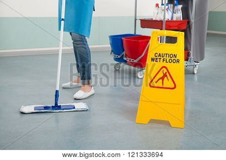 Female Janitor Mopping Corridor With Caution Sign