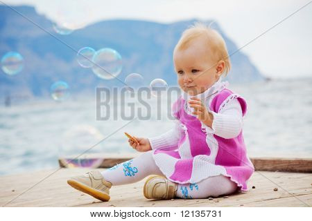 Portræt af lille søde baby pige ser på sæbebobler på kaj nær havet