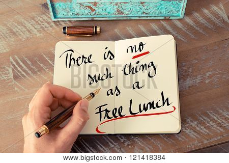 Retro effect and toned image of a woman hand writing a note with a fountain pen on a notebook. Handwritten text There Is No Such Thing As A Free Lunch as business concept image