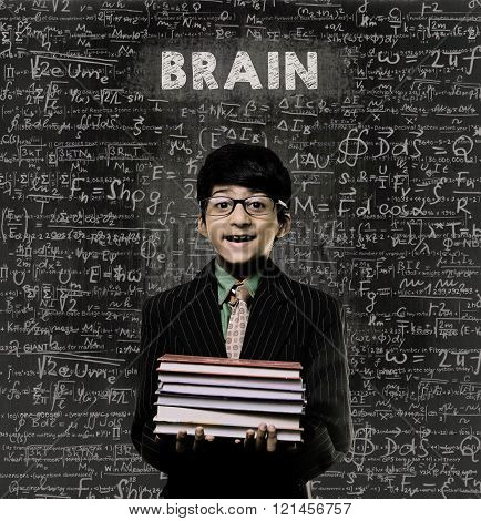 Cute Intelligent Little Boy Holding Book And Wearing Glasses Standing Before A Chalkboard Chemical Formulas Are Written On Board With The Chalkboard Typography Of The Word BRAIN