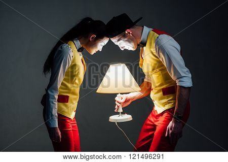 studio shot of two mimes isolated on a gray background. muffled light. look at the lamp