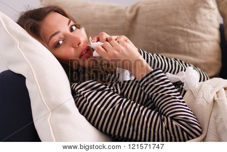 Portrait of a sick woman blowing her nose while sitting on the sofa