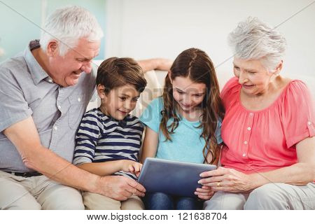 Senior couple and their grand children using digital tablet in living room