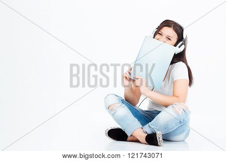Casual woman sitting on the floor in headset and book isolated on a white background