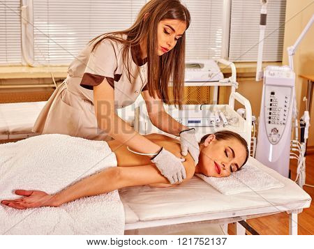 Young white  woman  receiving electric massage at beauty salon. Beautician wearing electricity gloves. In room is device for hardware cosmetology. Relax massage.
