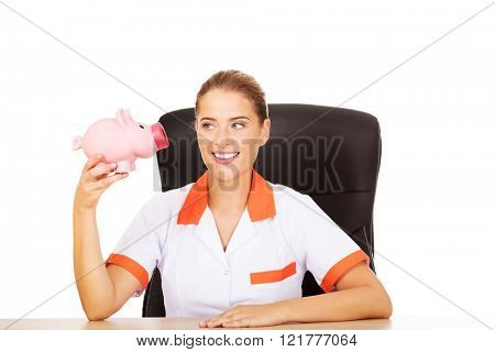 Smile doctor sitting behind the desk and holding a piggybank