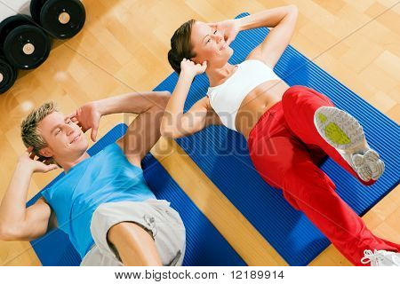 Paar mit bunten Kleider machen Sit-ups in der Turnhalle