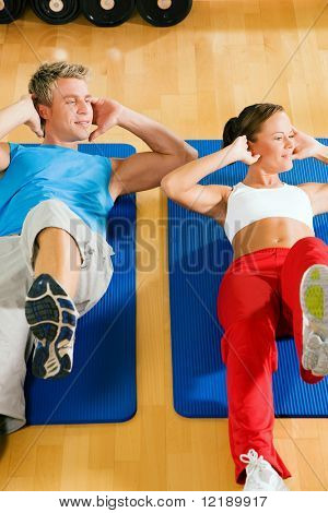 Paar mit bunten Kleider machen Sit-ups in der Turnhalle