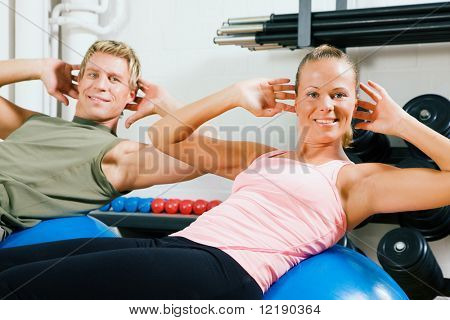 คู่ที่ทำ situps บนลูกบอลออกกำลังกายเป็นการฝึกในโรงยิม