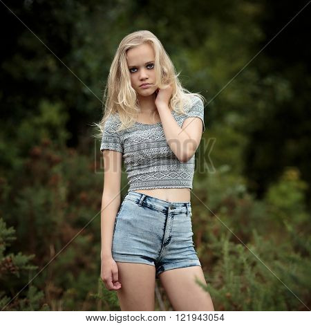 Location portrait of a beautiful young blond teenage girl alone in the woods wearing denim shorts looking in the camera.