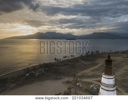 drone view of lighthouse on the shore at sunset time behind the mountains