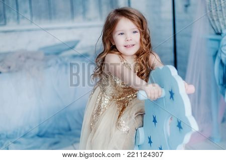 girl riding a toy wooden horse in his room and smiles