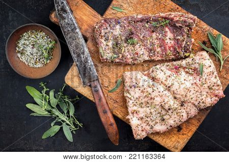 Cured wild pork belly with spices as top view on an old cutting board 