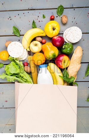 Grocery shopping concept. Different food in paper bag on wooden background.  Flat lay