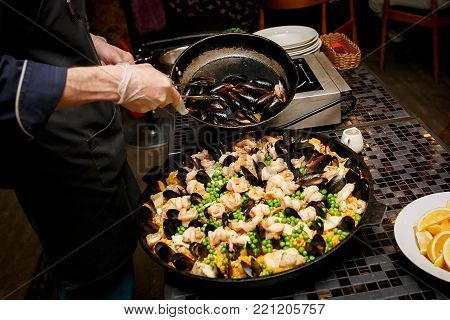 Cooking and making traditional Spanish Paella in iron cast pan. Preparing big paella, the chef adds mussels
