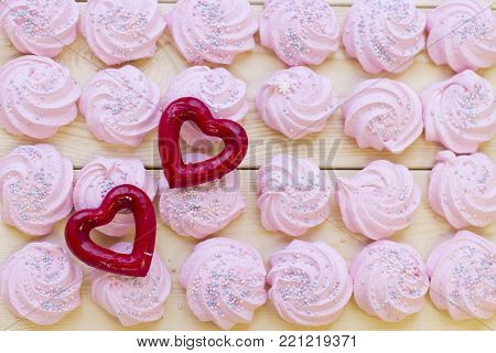 Pink marshmellows for Valentine's Day and red hearts on a wooden boad, top view