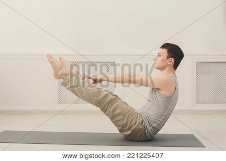 Young man practicing yoga with gymnastic mat, making corner stretching exercise, copy space