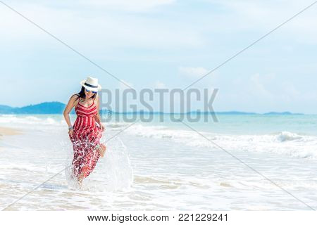 Summer Day.  Smiling woman wearing fashion summer beach having fun playing splashing water in freedom on the sandy ocean beach. Happy woman enjoy and relax vacation.  Travel Concept.