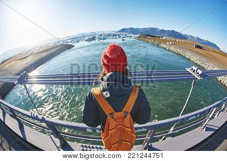 Cheerful woman wearing in red cup walks on the brige in Jokulsarlon Ice Lagoon, Iceland