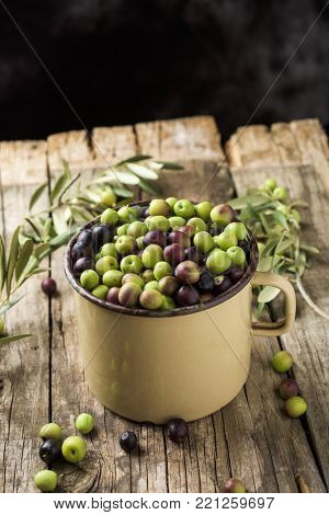 a handled enamelware pot full of arbequina olives from Catalonia, Spain, on a wooden rustic table, against a dark background with a blank space on top