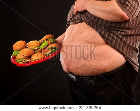 Man belly fat with hamberger fast food. Breakfast for overweight person. Chronic obesity. Person reduced consumption of hamburgers on black background.