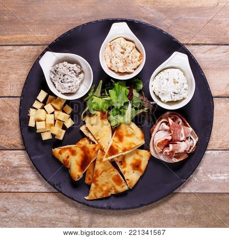 A plate with appetizers from the chef. Salads and fresh tortillas on a large ceramic plate. Salad dressing and design of dishes in restaurants and cafes.