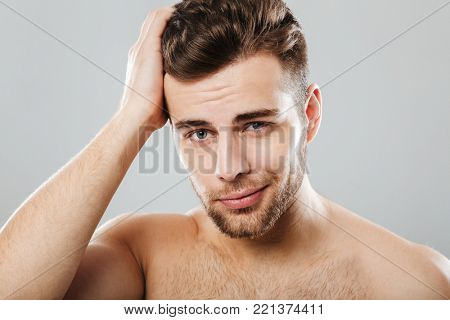 Close up portrait of a handsome man combing his hair with fingers isolated over gray background