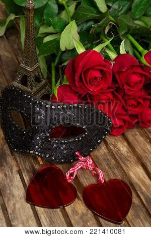 red fresh roses with black masque and two heart on wooden table