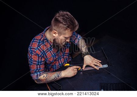 Tailor cutting leather with stencil knife on rubber board.