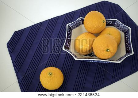 Several mandarin oranges in a pretty blue and white oriental dish on blue place-mat.